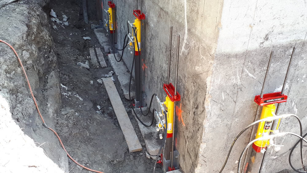 Réparation de fondation avec vérins hydrauliques rouges et jaunes.